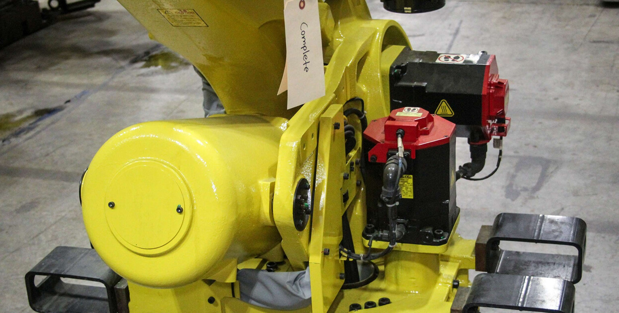 Yellow Fanuc robot with a &ldquo;Complete&rdquo; repair tag