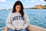 Female model wearing Baypointe Boston Ash mock neck sweatshirt with navy BOSTON lettering and thumb hole cuffs.