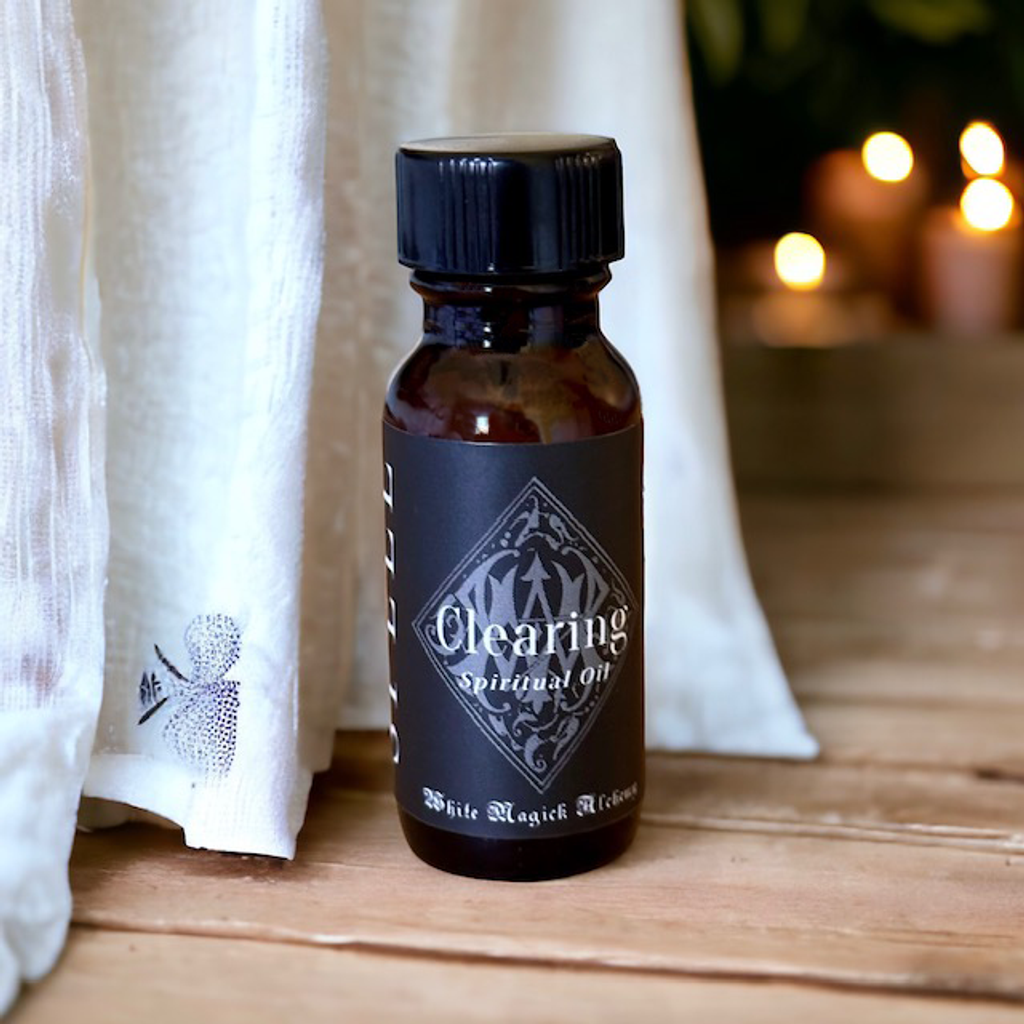 An amber bottle on a pine wooden floor with candles in the background with a black label that reads Clearing Spell Oil by White Magick Alchemy