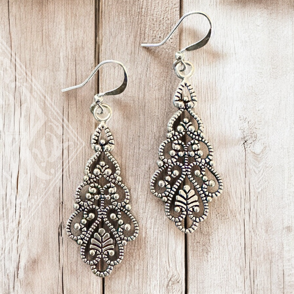 antique inspired filligree drop earrings in silver tone color on wood table 