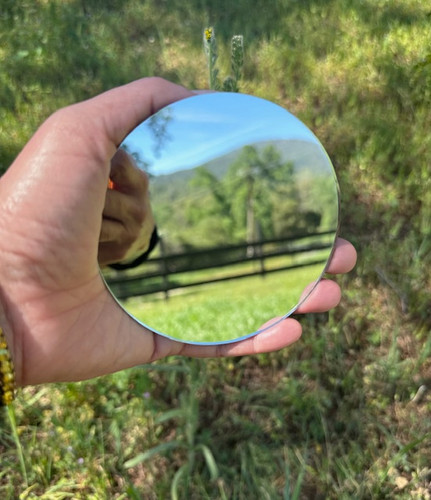 hand holding 4 inch round mirror plate reflecting mountain landscape
