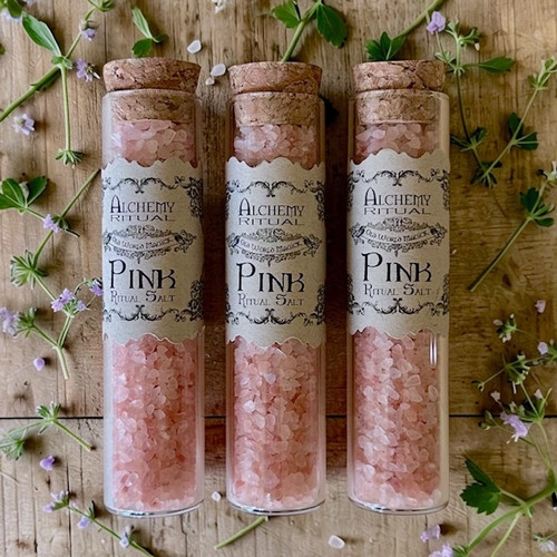 Pink ritual salt on a bed of herbs and flowers for witchcraft and spiritual tools and supplies