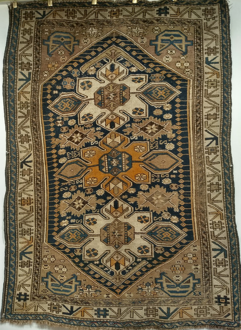 Late 19th Century Antique Caucasian Shirvan area rug. Hand-woven. Triple medallion with large diamond forms in ivory and orange. Navy blue background. Pale plum corner spandrels with "face drawings." Ivory color border with geometric designs in yellow, brown, and navy.