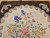 Vintage American hand-hooked floral rug from the early 1900s in brown, ivory, purple, pink, and blue with a wide brown border in a near-square format, The Persian Knot Gallery, SKU: 1443