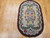 Oval vintage American hand-hooked floral rug from the early 1900s in ivory, green, red, and blue with a brown border, The Persian Knot Gallery, SKU: 1447