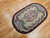 Oval vintage American hand-hooked floral rug from the early 1900s in ivory, green, red, and blue with a brown border, The Persian Knot Gallery, SKU: 1447