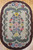 Oval vintage American hand-hooked floral rug from the early 1900s in ivory, green, red, and blue with a brown border, The Persian Knot Gallery, SKU: 1447