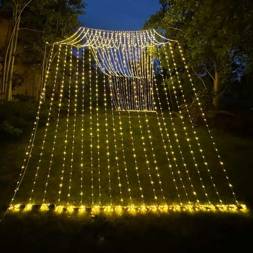 A stunning 10' x 30' warm white LED light curtain is gracefully displayed, with 3,600 tiny glowing lights cascading down in evenly spaced rows. The warm white light creates a soft, inviting ambiance, ideal for festive events or cozy décor. The expansive size provides a dramatic effect, covering a large walls, windows, or outdoor spaces. The gentle glow of the LEDs beautifully illuminates the surroundings, offering a magical, twinkling backdrop perfect for any occasion.
