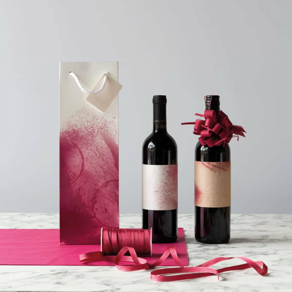 A bottle gift bag with two bottles next to it, sitting on some tissue and ribbon