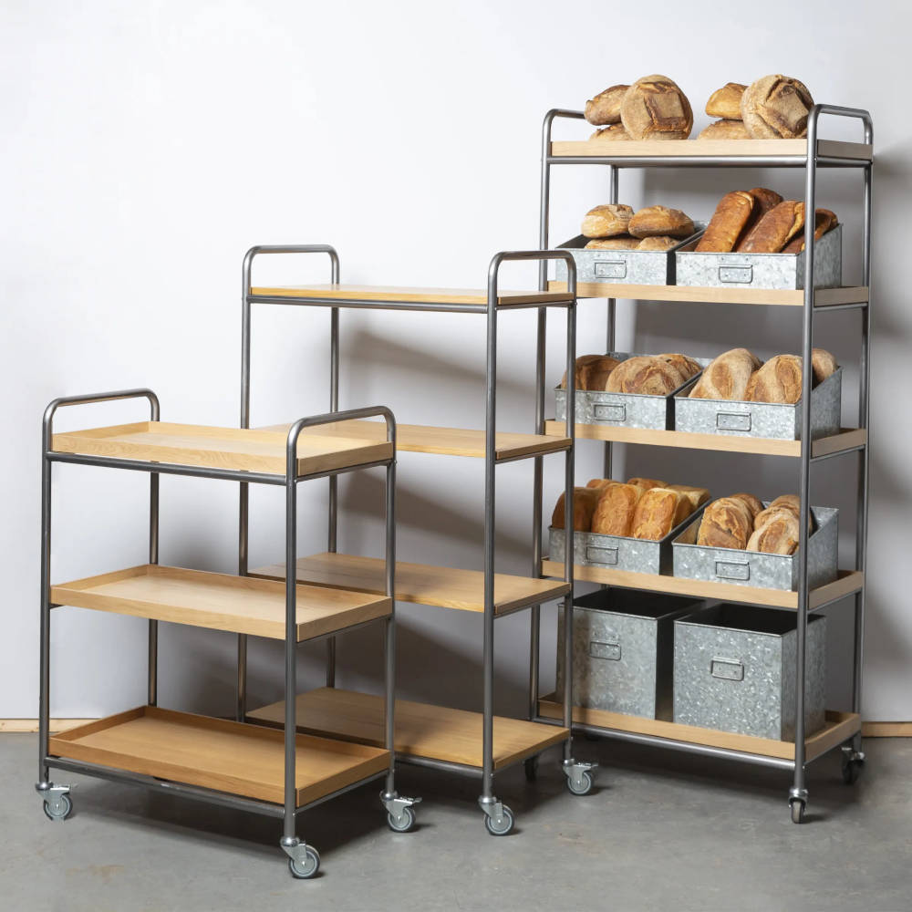 Three different sized shelves on wheels with the largest containing bread in metal boxes