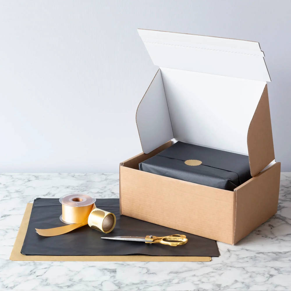 Brown box with a wrapped item inside with tissue paper, scissors and ribbon on a marble table