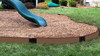 Frame It All Classic Sienna Curved Playground Border Kit 32' - 1" Profile, a curved brown plastic border installed around a playground area with wood mulch in a backyard setting.