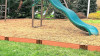 Frame It All Classic Sienna Straight Playground Border Kit 64' - 1" Profile, installed around the playground, creating a border between the grassy area and the play zone with a natural wood appearance. Frame It All Classic Sienna Straight Playground Border Kit 64' - 1" Profile, installed around the playground, creating a border between the grassy area and the play zone with a natural wood appearance.
