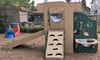 Strictly For Kids Deluxe Challenger 25 Wave Style Playground Structure, Natural or Bright, outdoor playground equipment with slide, climbing wall, and play panel, in a backyard with trees and houses. Strictly For Kids Deluxe Challenger 25 Wave Style Playground Structure, Natural or Bright, outdoor playground equipment with slide, climbing wall, and play panel, in a backyard with trees and houses.