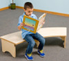 Playscapes Reading Retreat Bench, a child sitting on a curved wooden bench reading a book in a classroom setting.