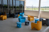 Playscapes Amped Chair, colorful modern plastic chairs and stools on a patio with a glass wall and outdoor view.