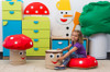 Novum Toadstool Soft Stool & Table for Kids, colorful mushroom-shaped children's furniture set with a girl sitting on a red cushion, surrounded by themed storage units and playful decorations.