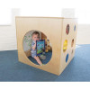 Whitney Brothers Whitney Plus Porthole Playhouse Cube, a wooden children's playhouse with circular cutouts and a large porthole opening, featuring a young child sitting inside with toys and a book.