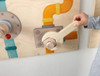 HABA Pro Mechanic Sensory Wall Panel, interactive wooden wall panel featuring a hand crank, colorful pipes, and mechanical components for sensory play and fine motor skill development.
