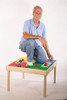 Synergy Management Fun Builder Wooden DUPLO® Table - 32" x 32", elderly man kneeling and playing with colorful DUPLO® blocks on a wooden activity table.