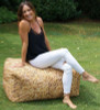 Playscapes Woodsmen Naturescape Straw Bale Bench, woman sitting on straw bale outdoor furniture in a garden setting.