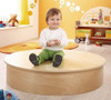 HABA Pro Sensory Bath with Lid, a child sitting on a round wooden sensory bath in a colorful playroom.