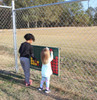 Infinity Playgrounds Connect 4 Playground Game, children playing connect 4 game outside near a chain link fence.