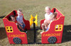 Infinity Playgrounds Infinity Express Caboose Outdoor Climber, colorful red and yellow outdoor playground equipment with four children playing inside on a grassy field.