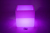 TickiT Sensory Mood Light Play Cube, illuminated cube emitting multicolored purple and pink glow with remote control in front of it.
