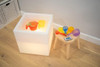 TickiT Sensory Mood Light Play Cube, illuminated cube with colorful silicone scoops and a remote control on a small wooden table, in a playroom setting.