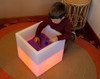 TickiT Sensory Mood Light Play Cube, a white illuminated cube with a colorful glow, used for sensory play by a child inside it.