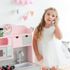 Teamson Kids Little Chef Florence Pink Play Kitchen with Accessories, a doll girl in a white dress talking on a toy phone beside a pink play kitchen set with a clock, sink, and microwave, in a pastel-colored room with heart and cloud decorations.