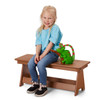 Jonti-Craft EverPlay Small Outdoor Bench, a wooden outdoor children's bench with a young girl seated on it, smiling with a green toy chameleon beside her.