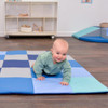 Children's Factory Patchwork Activity Play Mat, Tranquility, with a baby crawling on it in a playroom setting.