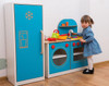 Moje Bambino Amelia Kitchen Play Refrigerator, a colorful children's play kitchen set with a refrigerator, stove, and countertop, featuring bright blue, red, and yellow details, with a young girl playing.