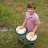 Playmore Designs DouBBle Play Drum Table, a young boy playing drums outdoors on a green table with two drum pads.
