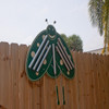 Playmore Designs Butterfly Music Chimes, decorative butterfly-shaped outdoor musical instrument mounted on a wooden fence with palm trees and a cloudy sky in the background.