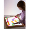 Guidecraft Ultra-Slim LED Light Activity Tablet, a young girl playing with colorful magnetic shapes on a backlit touchscreen surface.