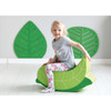 Moje Bambino Soft Foam Rocking Seats, a green foam rocking seat shaped like a leaf with a young girl sitting on it, smiling in a bright room with green leaf wall decorations.