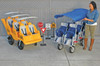 Angeles 6 Passenger BYE BYE BUGGY Daycare Stroller Bus, image showing a woman preparing a blue covered stroller for children next to a yellow BYE BYE BUGGY bus with six seats.