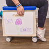 Angeles Mobile Teacher Stool - Assembled, a compact and portable wooden stool with a blue cushioned seat and wheels for easy mobility, shown with a whiteboard attached displaying a colorful drawing and words.