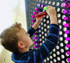 LiteZilla Giant Lite Brite - 46 x 38 inches, child creating colorful light design on large grid with colorful translucent pegs.