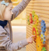 LiteZilla Kidworx Gizmo Wall Gears Wall Activity, a young girl interacting with colorful gear-shaped activity panels on a wall.