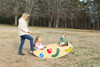Infinity Playgrounds Slayden’s Toddler Caterpillar Seesaw, children playing on a colorful saw-shaped seesaw with a woman supervising outdoors in a park.