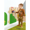 Moje Bambino Magnetic Decorations for Meadow Fence Sensory Wall, a child interacting with a colorful wooden and fabric rooster decoration on a sensory wall.