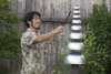 Freenotes Standard / Inclusive Mallet, Black 80A with 33-inch cable, being used by a man to strike a musical instrument outdoors in a garden setting.