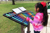 Freenotes Serenade Outdoor Chimes, a colorful musical instrument with various musical notes, being played by a girl outdoors.