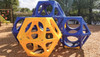 World Klass Play Ruby Qube Climbing Cube Cluster, colorful outdoor play equipment with interconnected geometric climbing structures in yellow and blue, set on a play area with wood chip surface.
