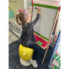 Playscapes Kids Adjustable Pivot Stool - Tall, a child sitting on a yellow adjustable stool while writing on a whiteboard.