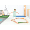 Moje Bambino Rollers Balancing Board, a young girl balancing on a wooden rollers board in a playroom with various play equipment around.